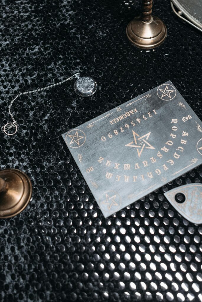 pexels-photo-7267484-7267484 Top view of a mystic Ouija board with pendulum on a textured black surface, creating a spiritual atmosphere.